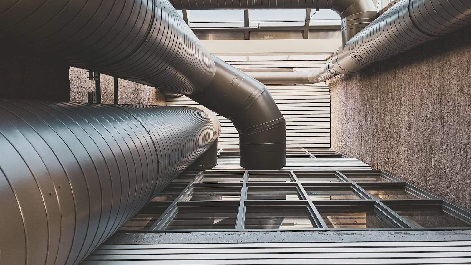 Large insulated ventilation ducts running along the outside of a building, seen from below.