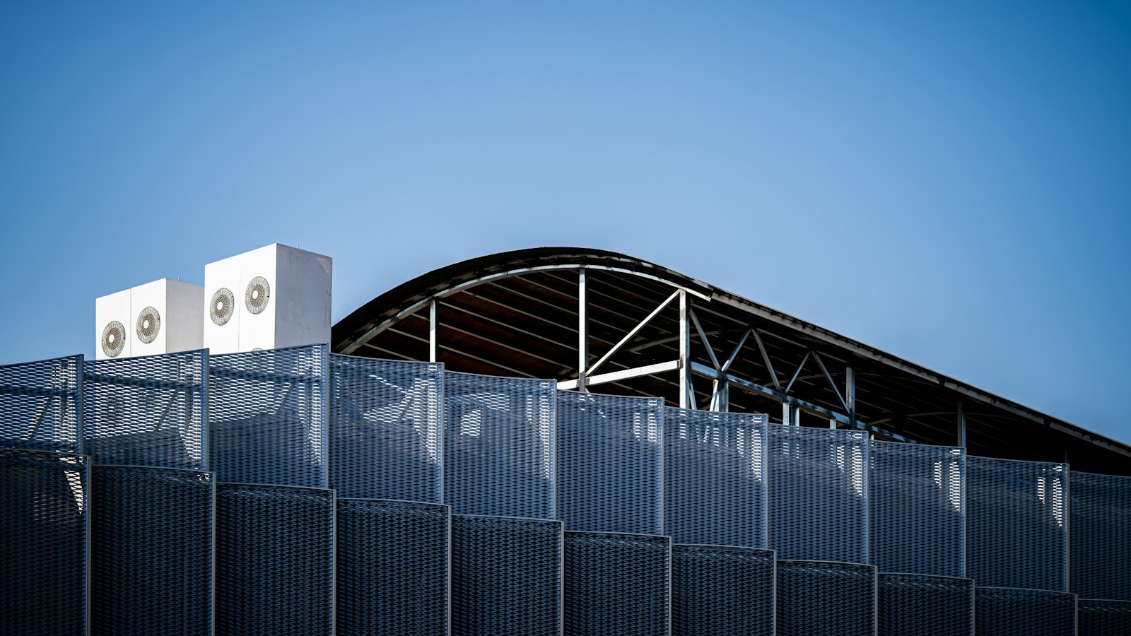 Rooftop cooling units above a building facade, against a clear sky.